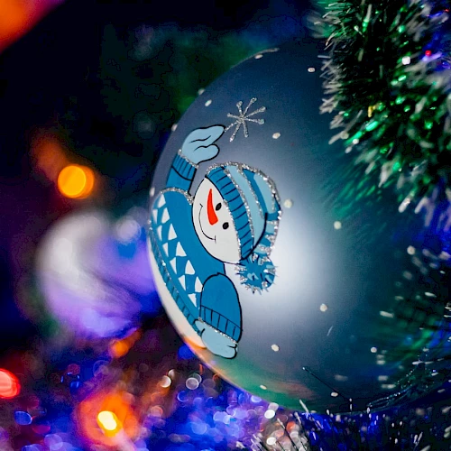 A Christmas tree ornament with a snowman design, surrounded by twinkling lights and green tinsel, is shown in the image.
