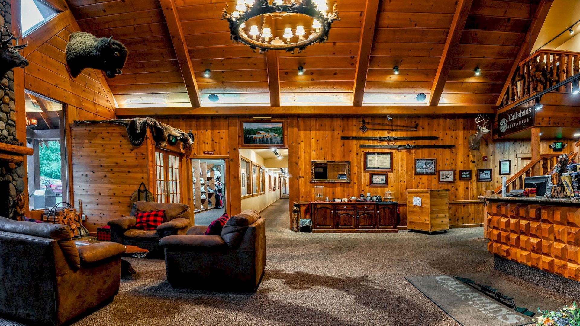 A cozy, rustic lodge interior with wooden walls, leather sofas, mounted animal heads, a chandelier, and various decorations.