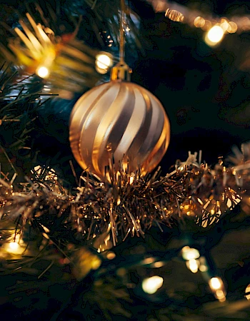 A decorated Christmas tree with a golden bauble, tinsel, and glowing lights creating a festive atmosphere.