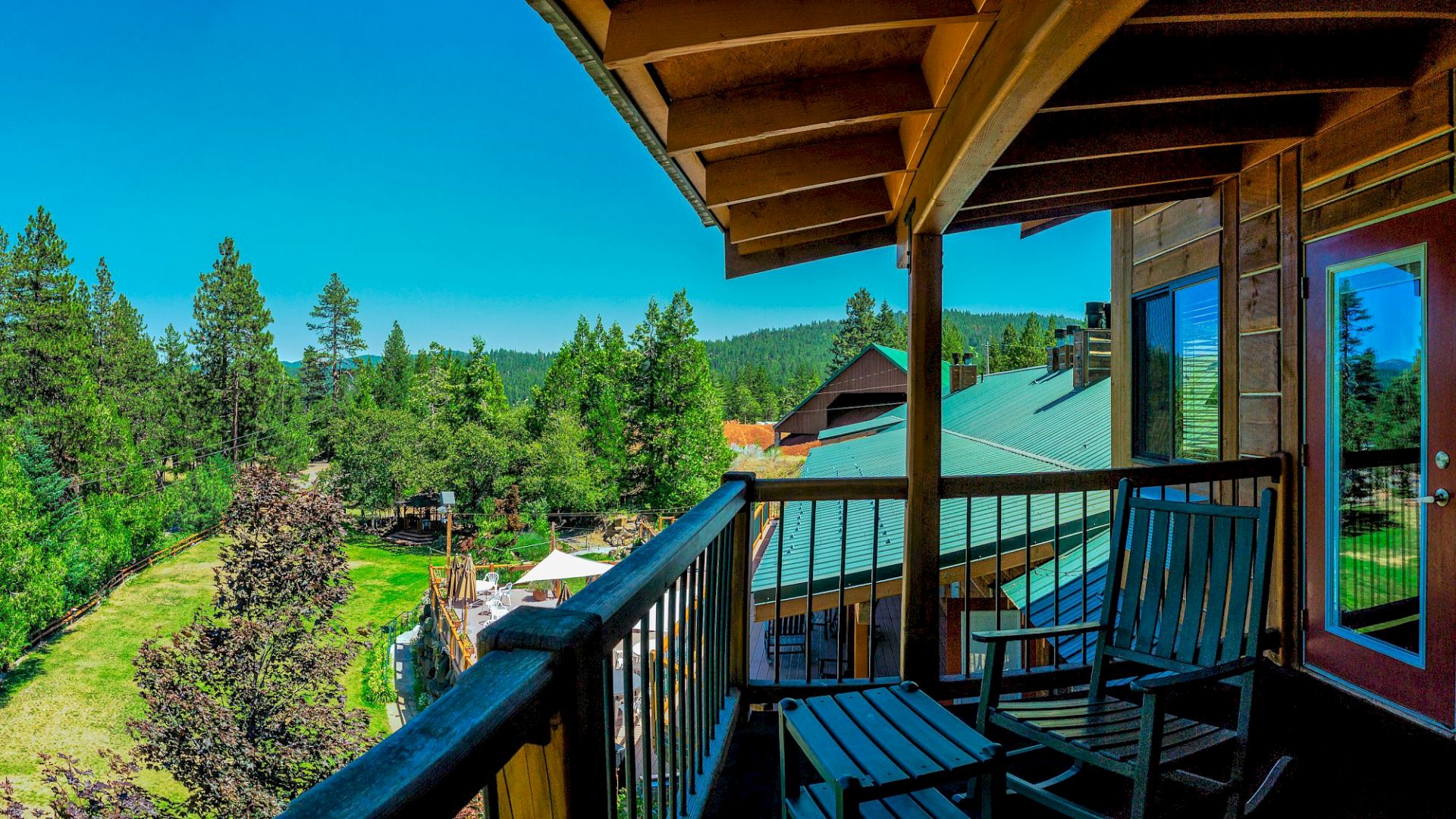 A wooden deck with chairs overlooks a forested landscape under a clear blue sky.
