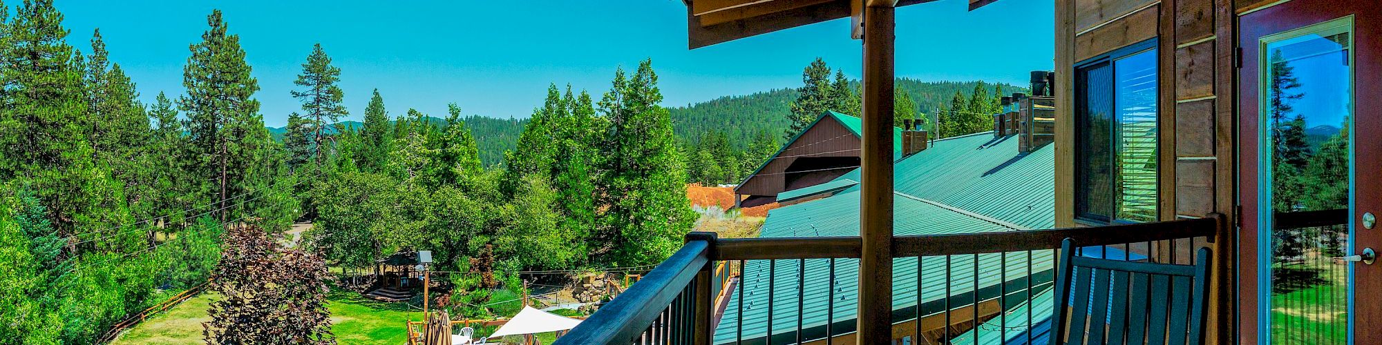 A wooden deck with chairs overlooks a forested landscape under a clear blue sky.