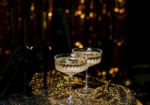 Champagne flutes glisten on a sequined table as warm fairy lights glow in the background, creating a festive, glamorous atmosphere.