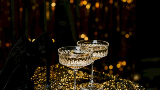 Champagne flutes glisten on a sequined table as warm fairy lights glow in the background, creating a festive, glamorous atmosphere.