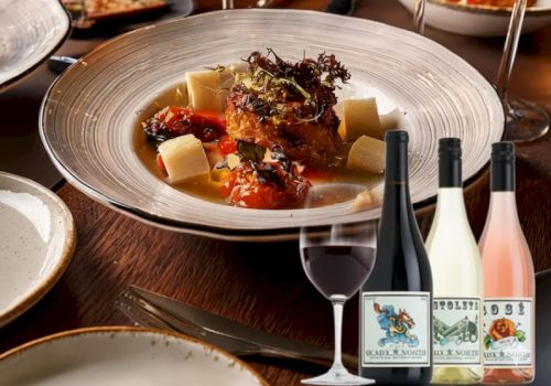 A fine dining scene with a plated main dish, several wine glasses, and bottles on a table, suggesting a sophisticated dinner with wine pairings.