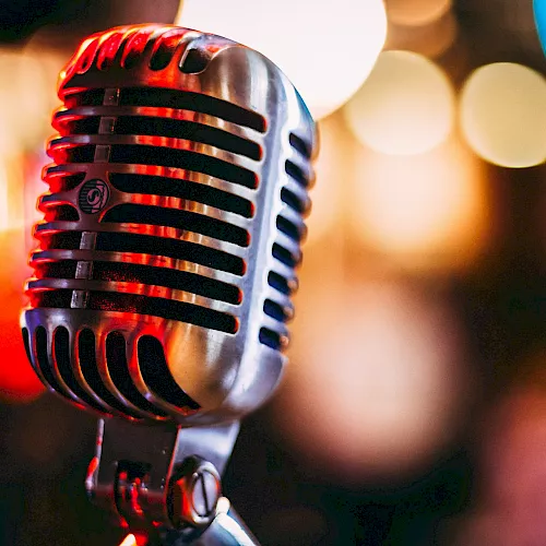 A close-up of a vintage-style microphone with red lighting and soft bokeh lights behind it, ready to capture vocals.