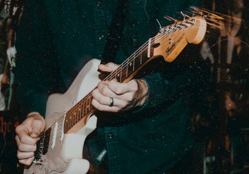 A person is playing an electric guitar or bass, gripping the fretboard as strings glow against a dark, moody background.