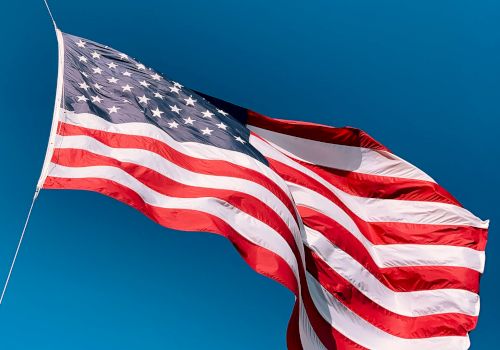 A United States flag waves in the wind against a clear blue sky, its stars and stripes filling the frame.