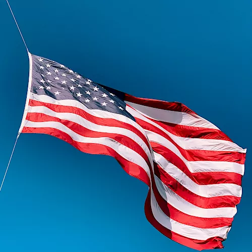 A waving United States flag with stars and stripes against a clear blue sky.