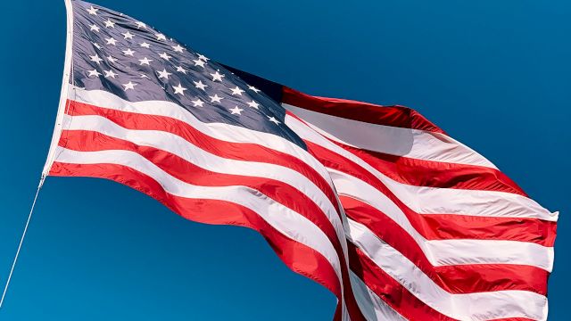 A waving United States flag with stars and stripes against a clear blue sky.