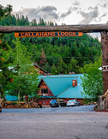 A rustic gateway labeled Callahan&rsquo;s Lodge arches over a forest road, with cars and signs pointing the way into the lodge.