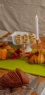 Autumn buffet table with lit candles, plates of pastries and cheese, plus Prosecco bottles and fall leaves on the green cloth.