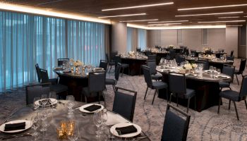 A banquet hall with round tables set for an event, featuring black chairs, elegant table settings, and soft ambient lighting from the ceiling.