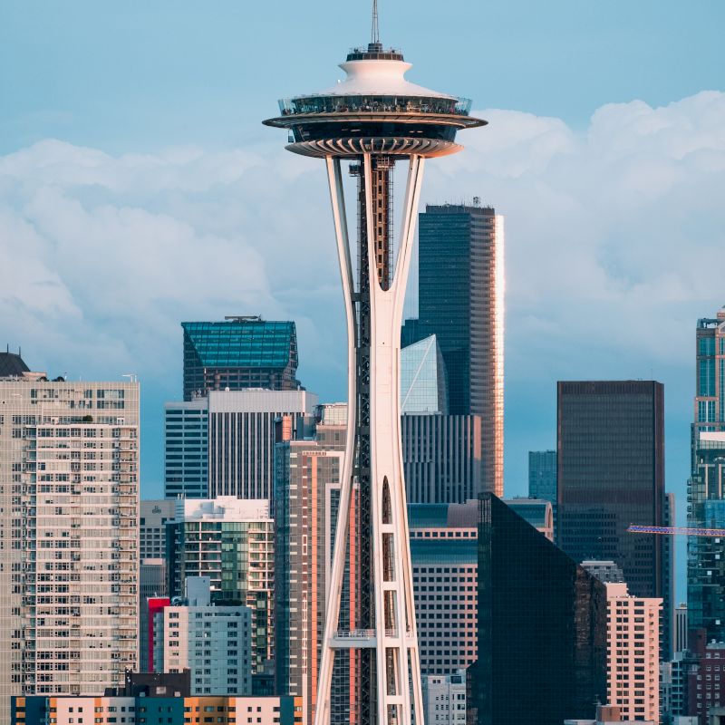 The image shows the Space Needle against a backdrop of skyscrapers and a cloudy sky, representing a cityscape, likely Seattle.