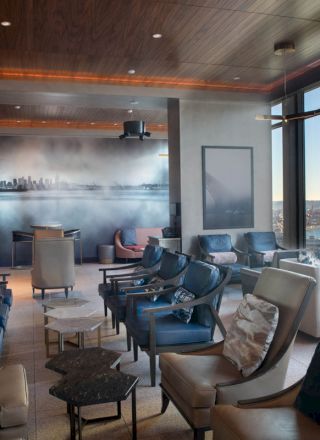 A modern, stylish lounge with comfortable seating, large windows showcasing a city and water view, and a mural on the back wall.