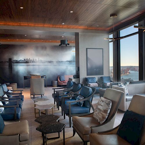 A modern lounge with comfortable seating, large windows with a view of the water, and city-themed wall art, offering a cozy and relaxed atmosphere.