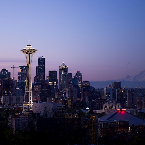 The image shows the Seattle skyline at twilight with the Space Needle prominently visible and Mount Rainier in the background under a clear sky.