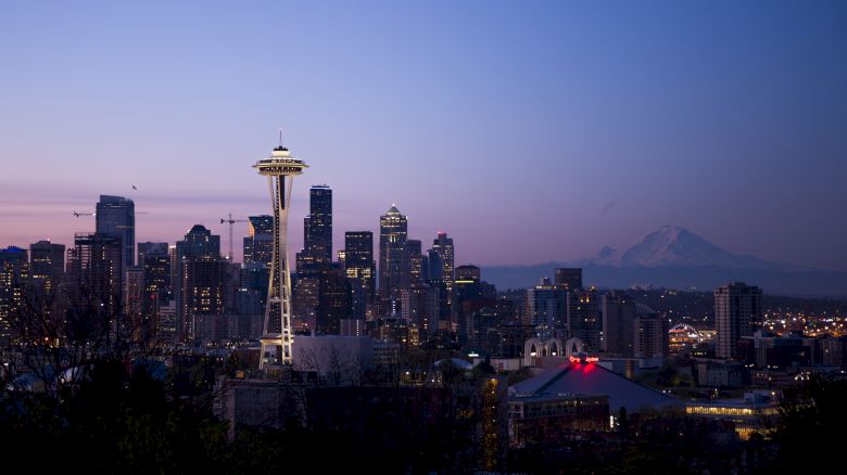 Seattle skyline at dusk featuring the iconic Space Needle, with Mount Rainier visible in the background under a twilight sky.