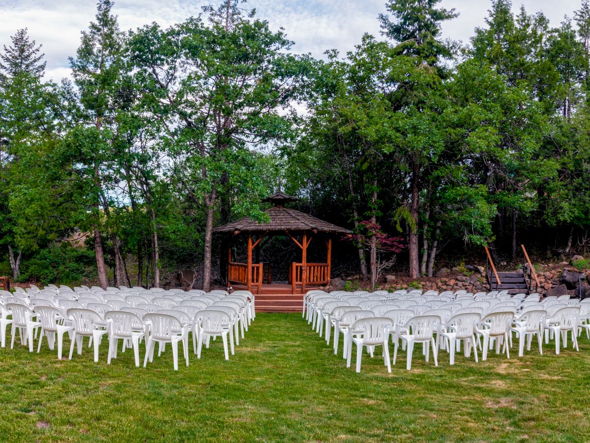 An outdoor wedding setup with white chairs arranged in rows facing a wooden arbor surrounded by trees and greenery ends the sentence.